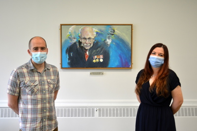 Man and woman beside portrait of captain Tom