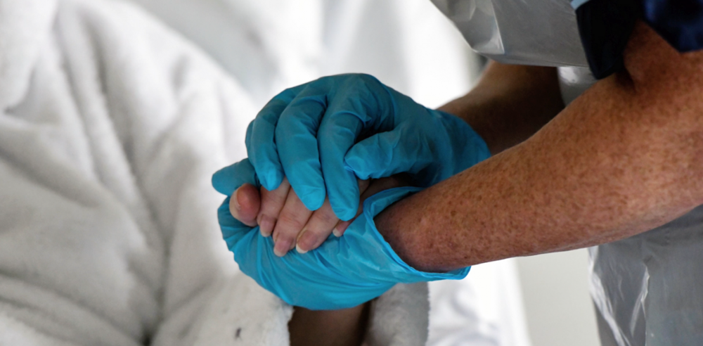 Gloved hands holding patients hand comforting