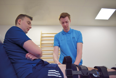 young guy sitting down with leg brace with physiotherapist