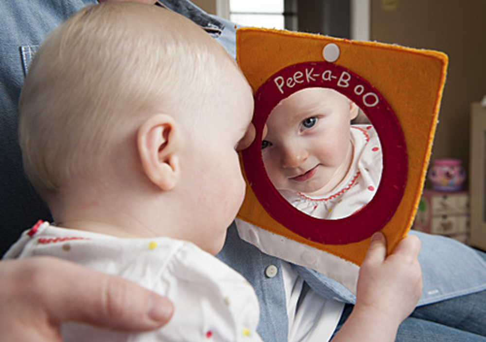 Baby looking in book mirror saying peek-a-boo
