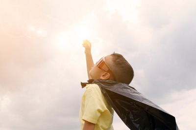 young boy looking at clouds like superman