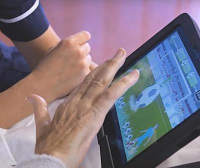 A digital tablet featuring interactive software called RITA, which stands for Reminiscence/Rehabilitation & Interactive Therapy Activities, being used by patient and member of nursing staff.