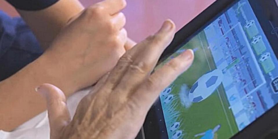 A digital tablet featuring interactive software called RITA, which stands for Reminiscence/Rehabilitation & Interactive Therapy Activities, being used by patient and member of nursing staff.